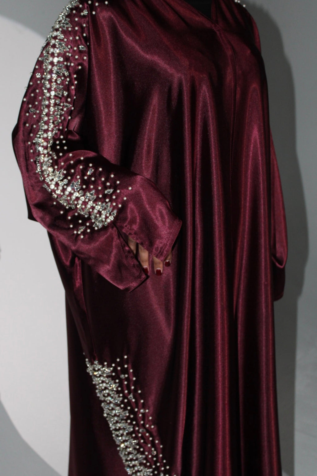 Maroon abaya with silver embellishments on sleeves and hem against a gray background