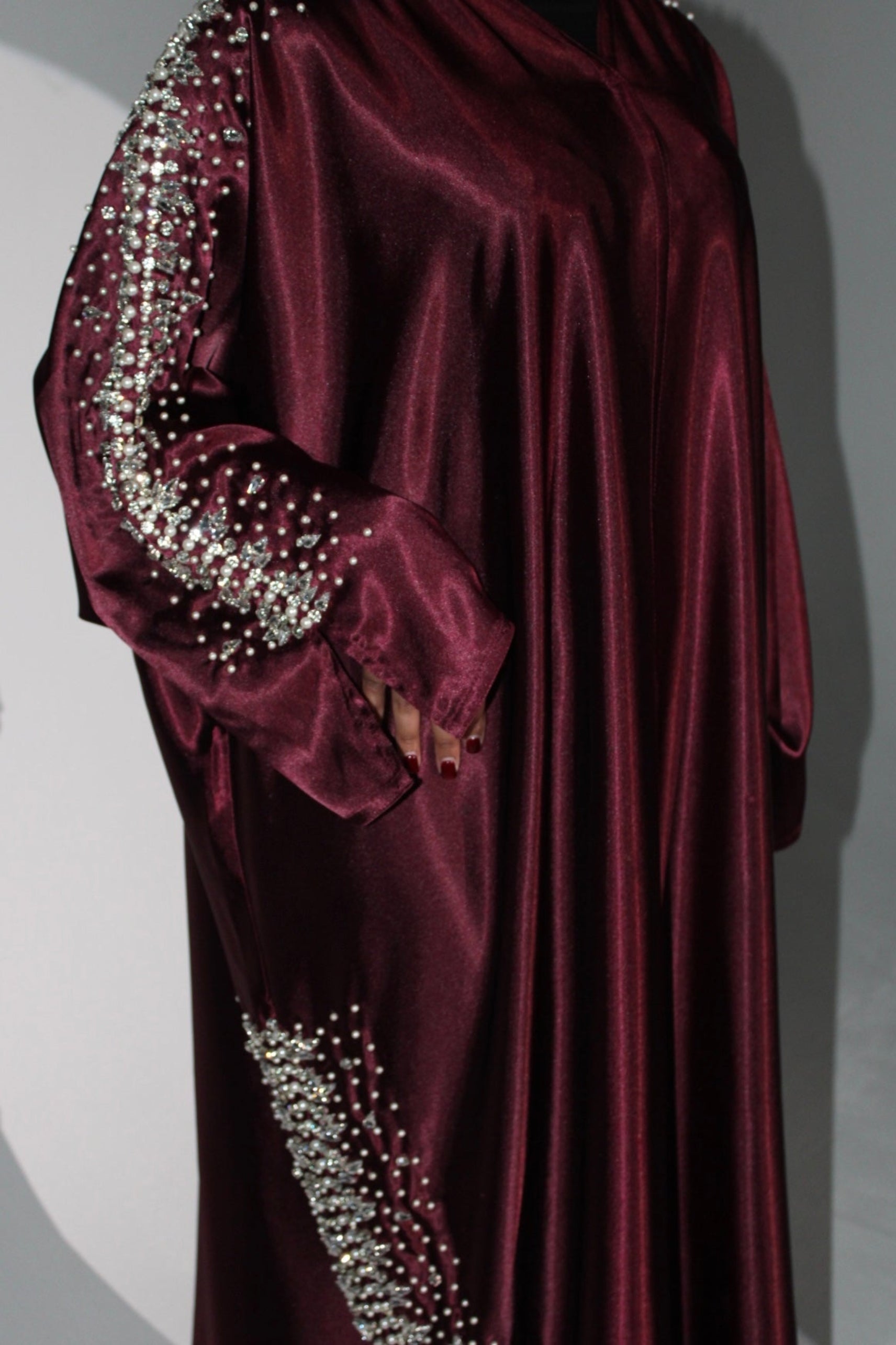 Maroon abaya with silver embellishments on sleeves and hem against a gray background