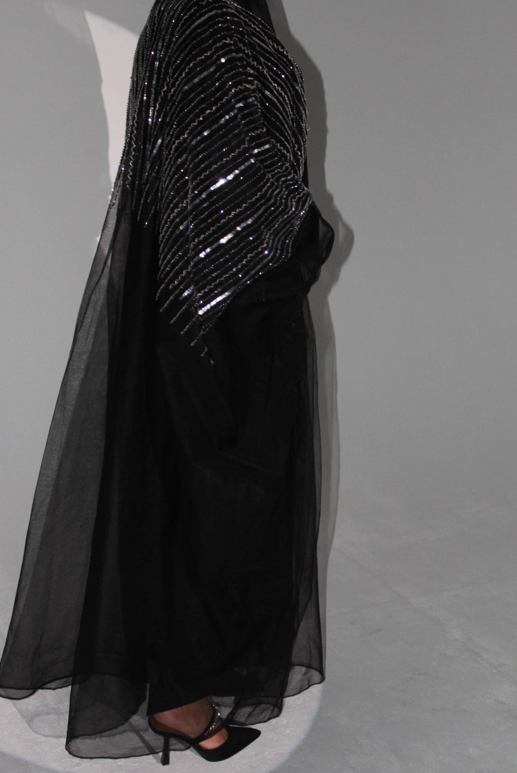Black evening abaya with sequin detailing on a mannequin against a gray background