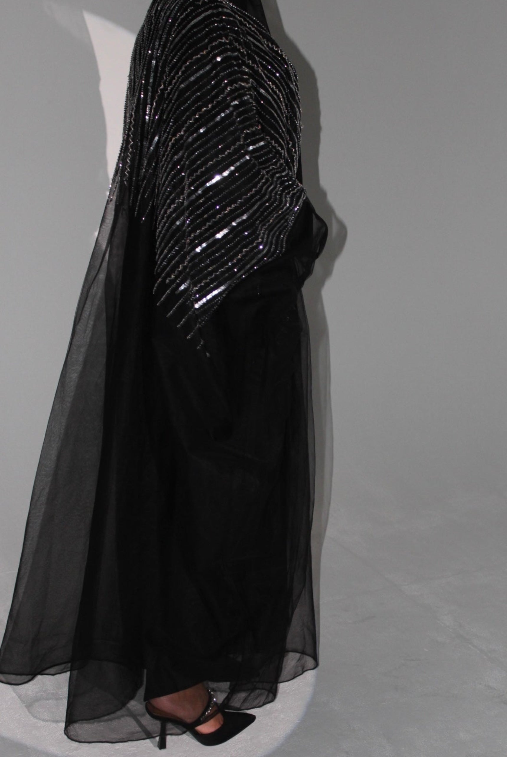 Black evening abaya with sequin detailing on a mannequin against a gray background