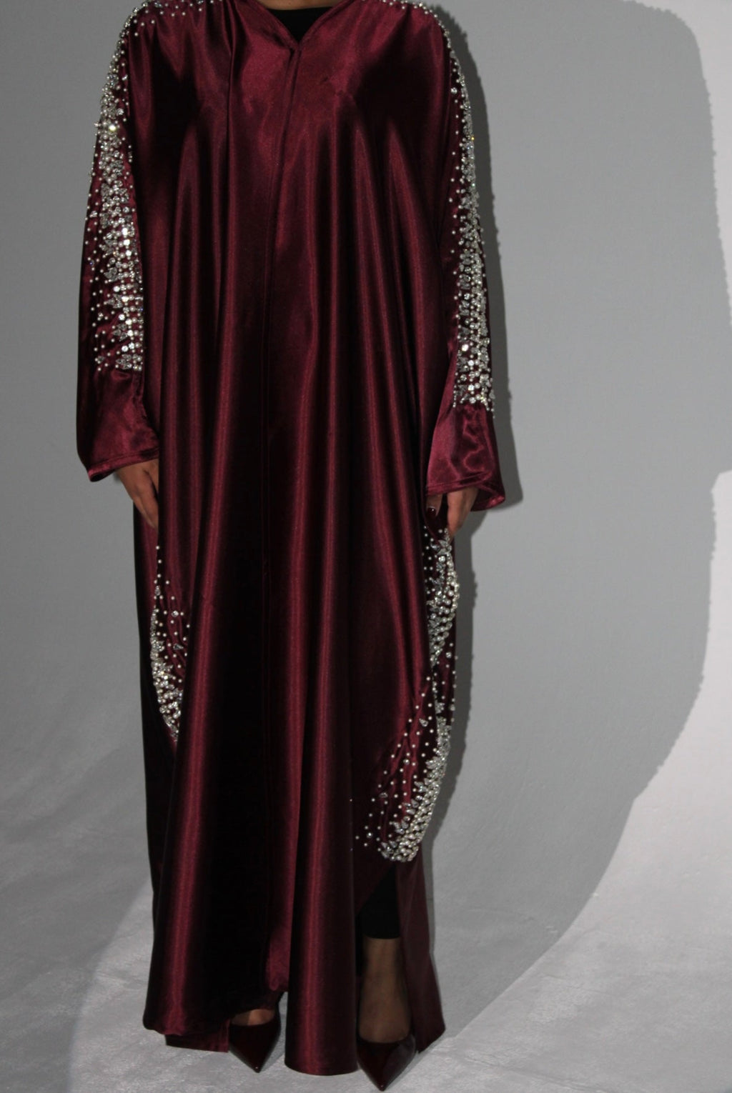 Maroon abaya with silver embellishments on sleeves against a gray background