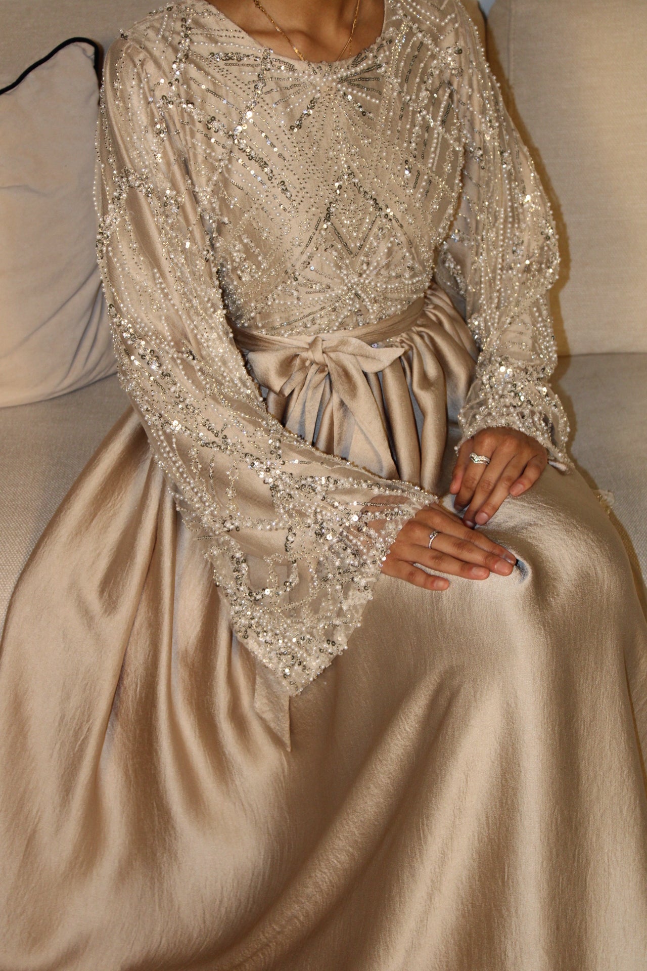 Close-up of a person wearing a beige dress with intricate beaded detailing.