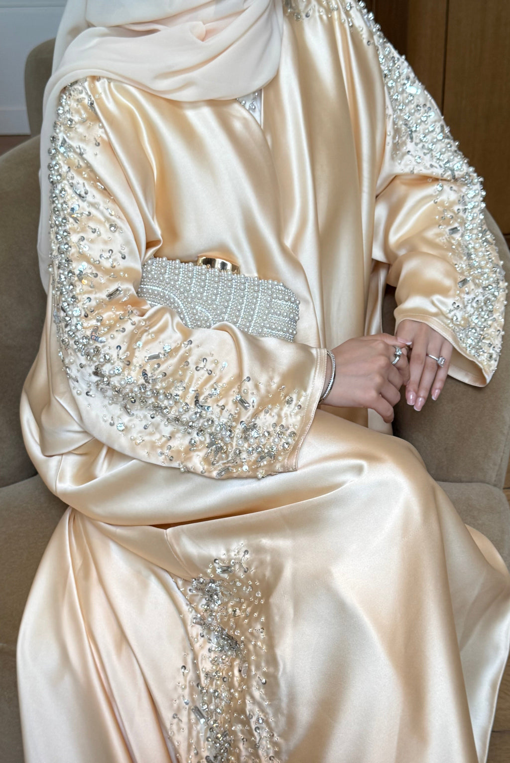 Person wearing a beige abaya with intricate beadwork sitting on a chair.
