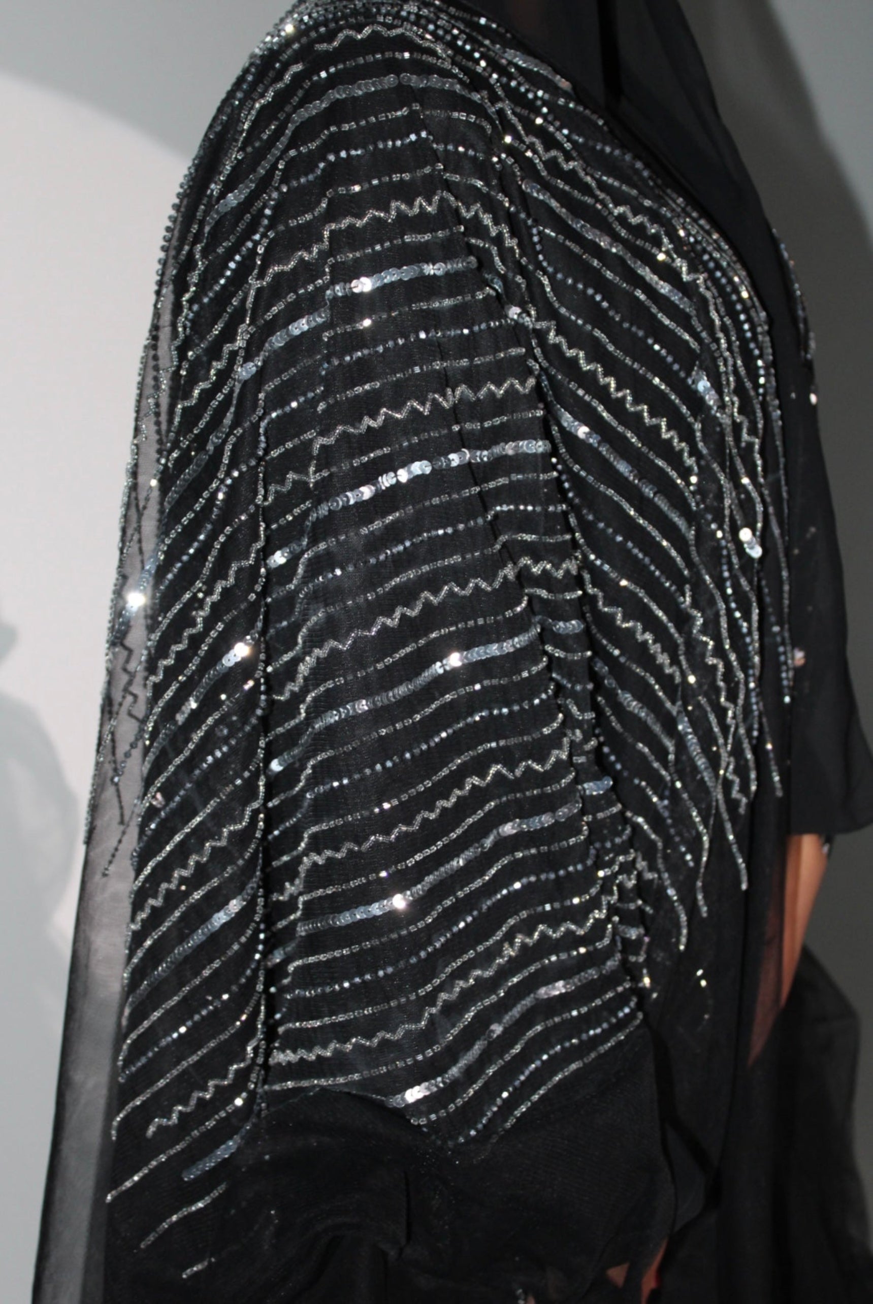 Close-up of a black abaya with silver sequin detailing on a plain background