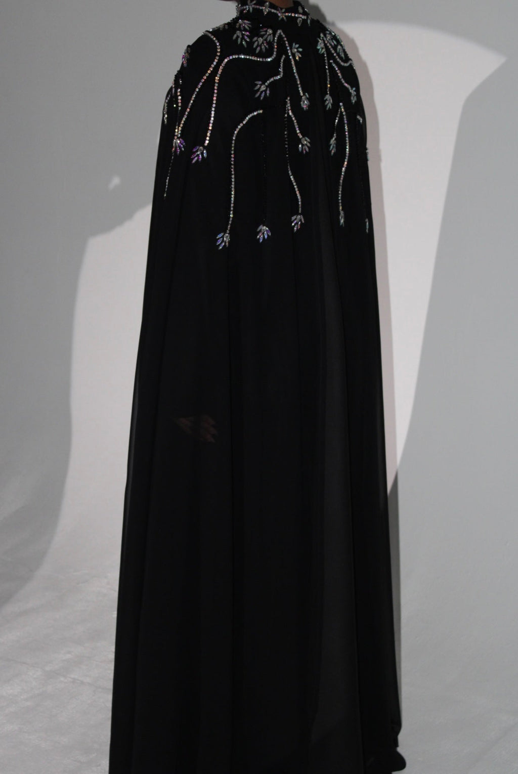 Black cape with intricate beadwork and abaya on a gray background