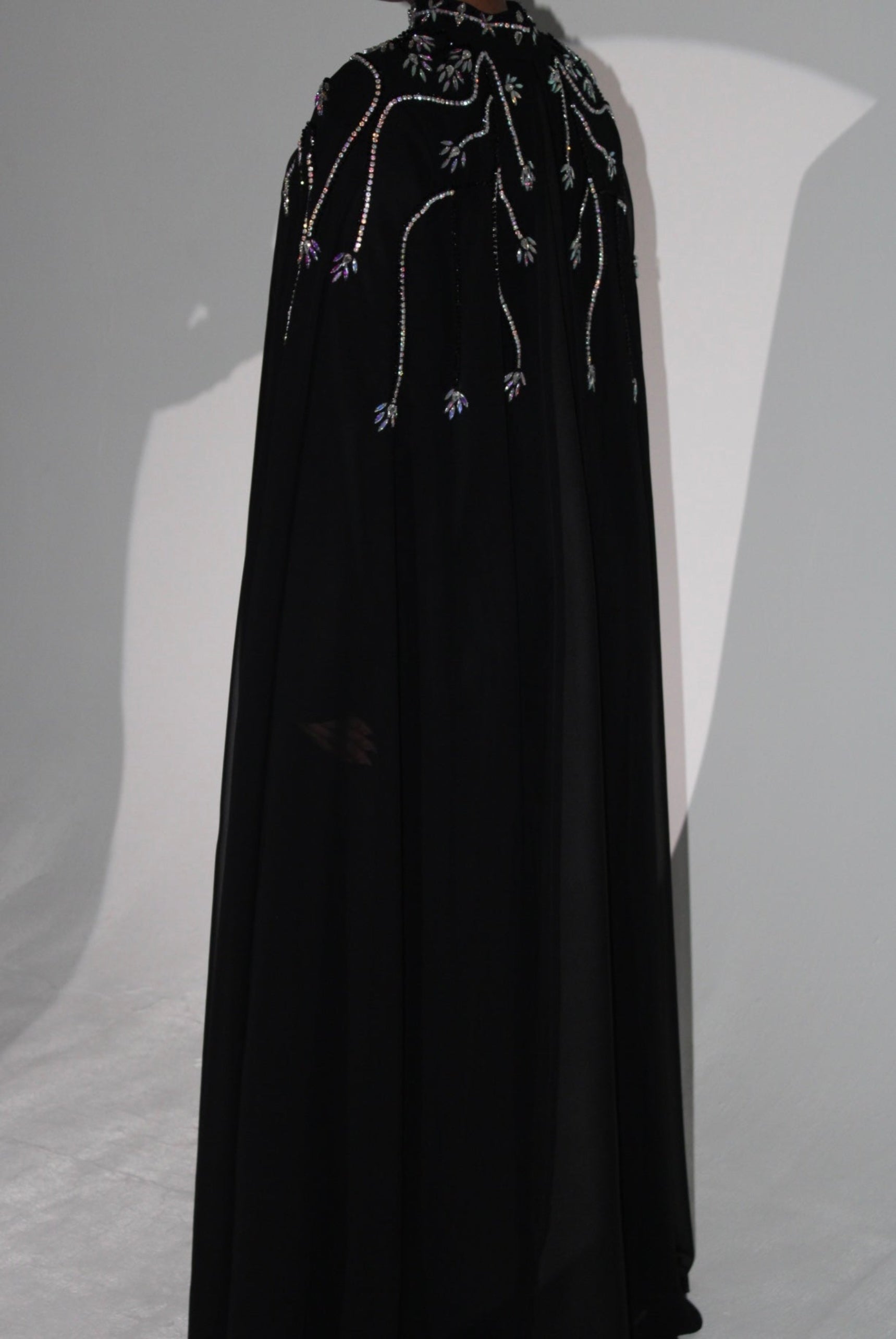 Black cape with intricate beadwork and abaya on a gray background