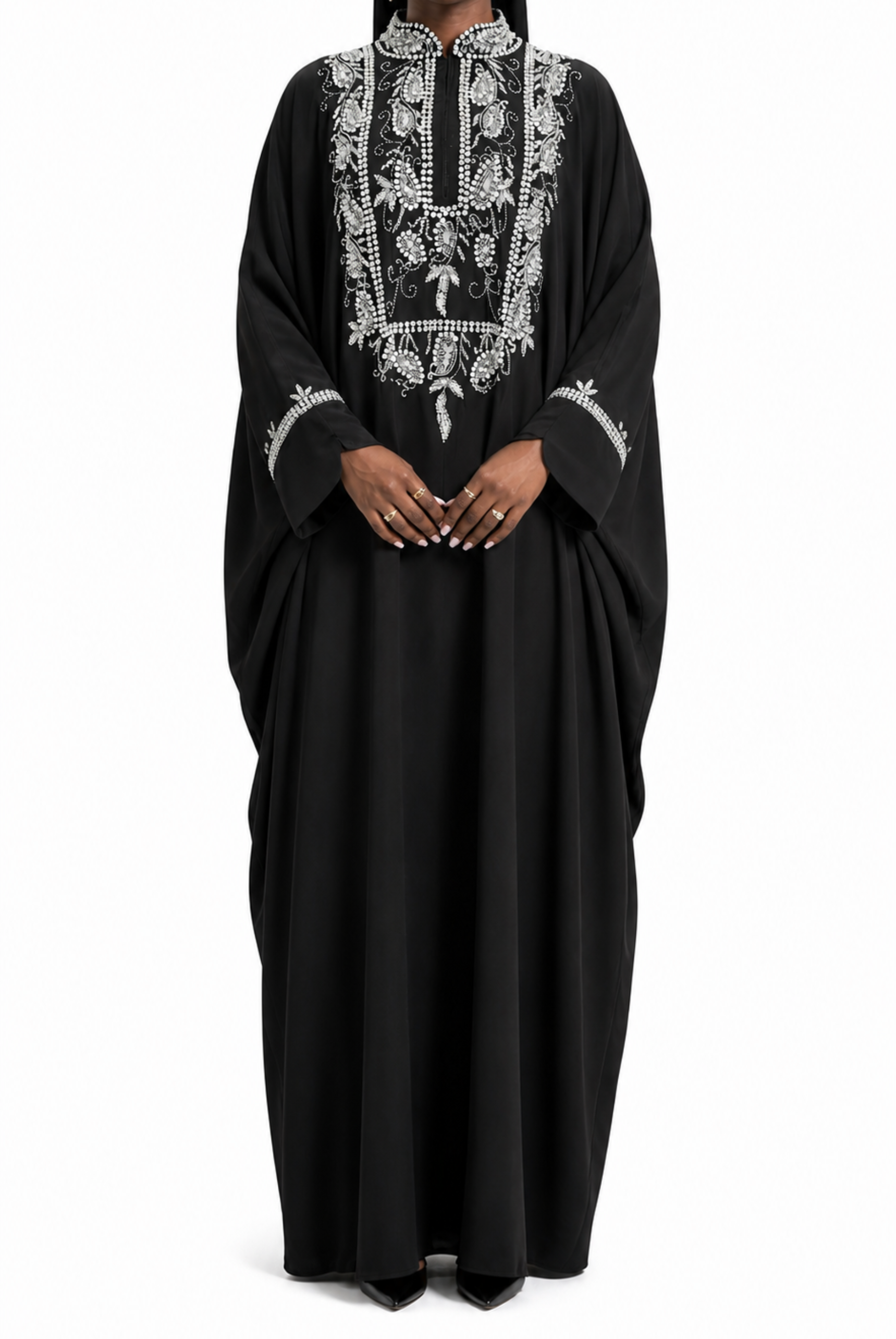 Woman wearing a black abaya with white embroidery on a white background