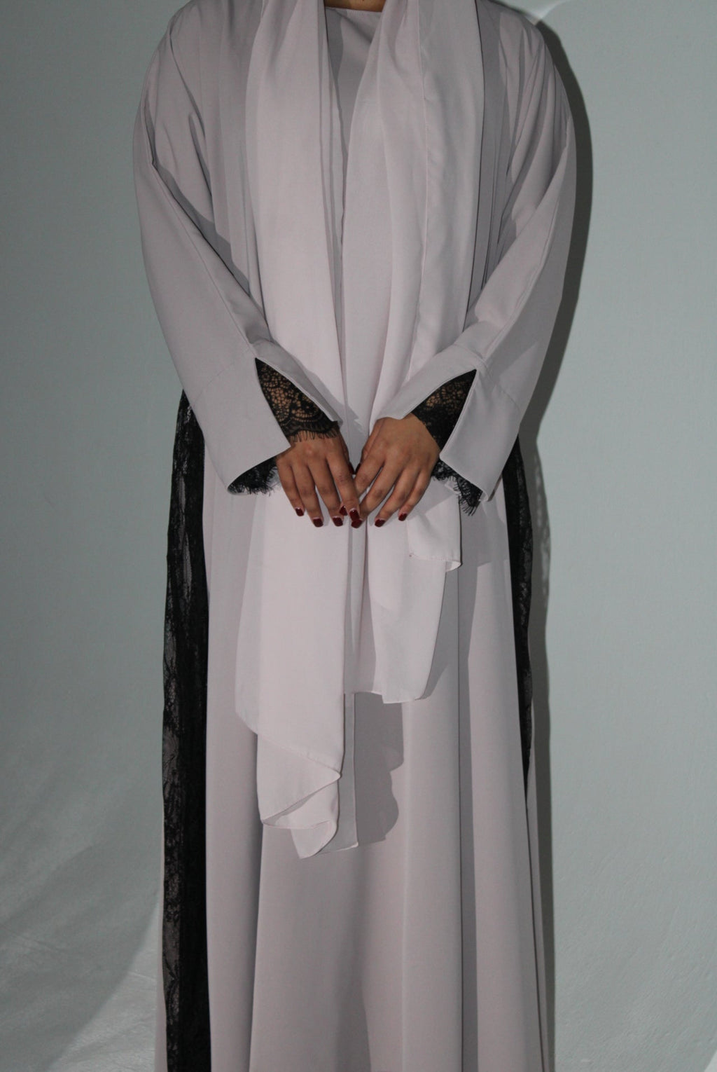 Person wearing a light pink abaya with black lace details on a plain background