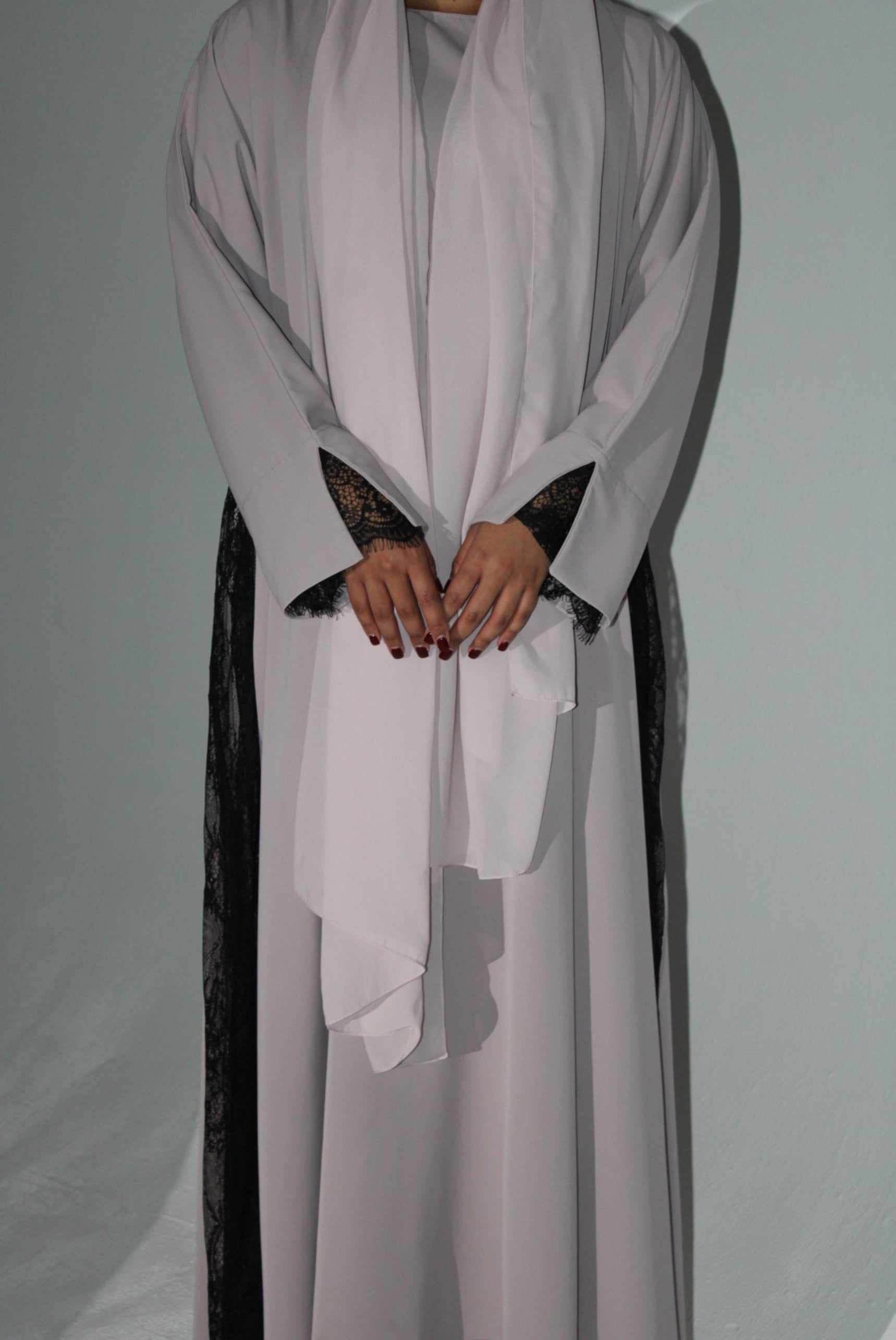 Person wearing a light pink abaya with black lace details on a plain background