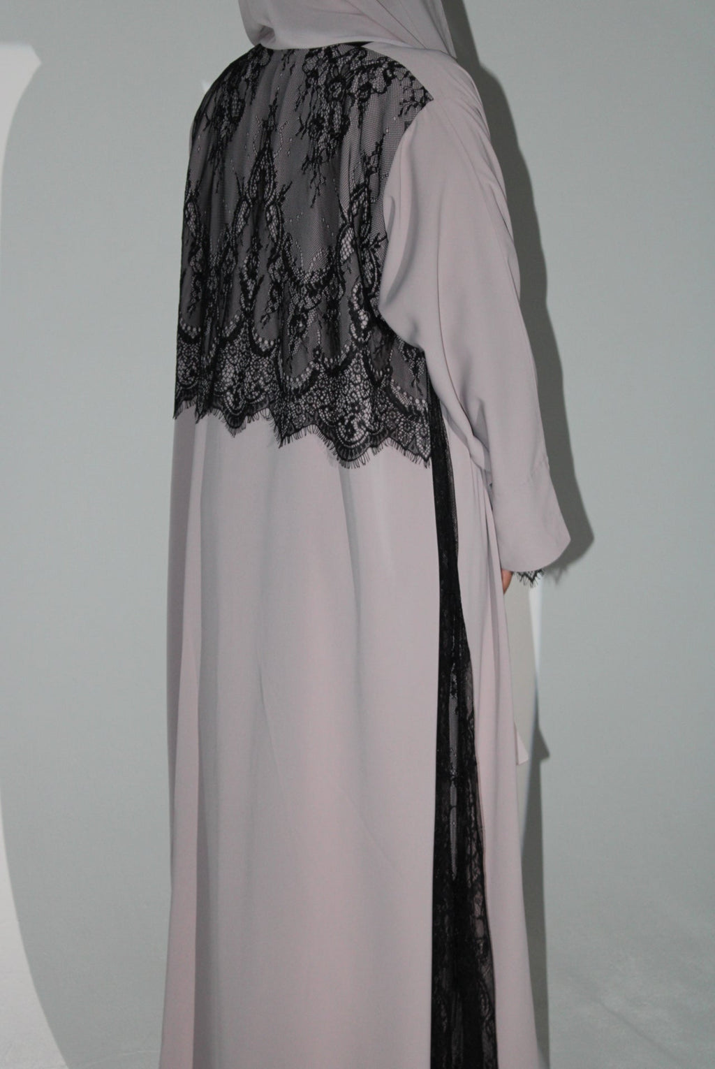 Light pink abaya with black lace detailing on a white background