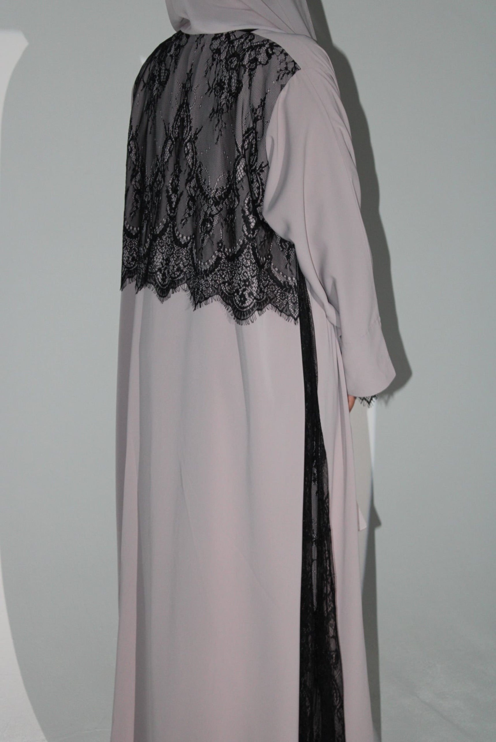 Light pink abaya with black lace detailing on a white background