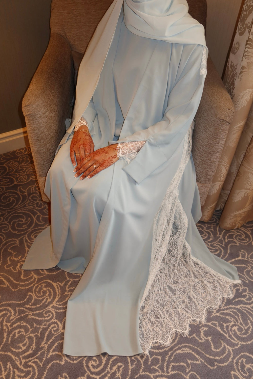 Person wearing a light blue dress with lace details sitting on a patterned chair.
